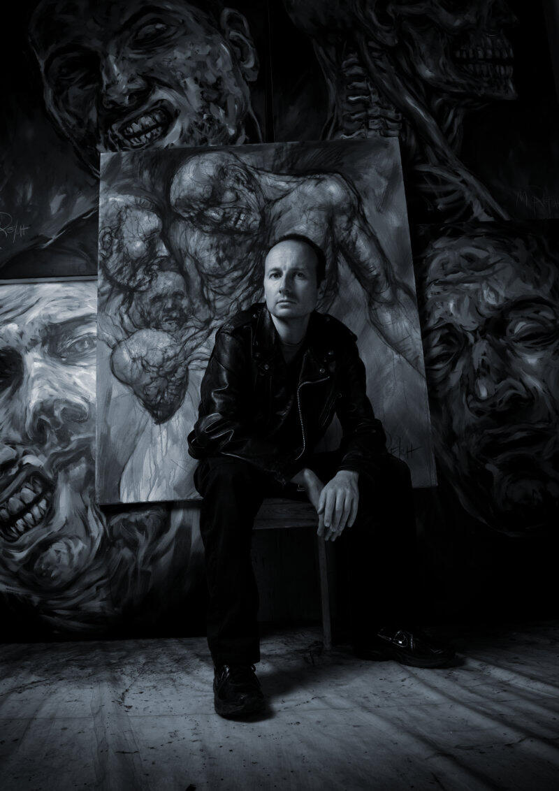 Photo of Marcel Reich · Artist Painter Black and white photo of artist painter Marcel Reich in front of his large-scale paintings, featuring a visceral, dark surrealism with a dystopic edge.